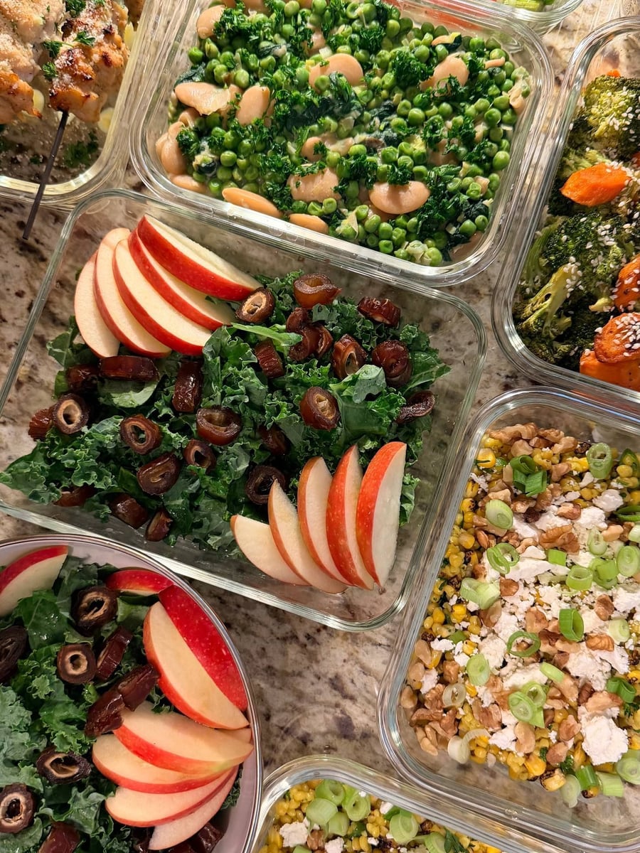 Apple slices fan across the shredded kale with halved dates, roasted broccoli and carrots beside it.