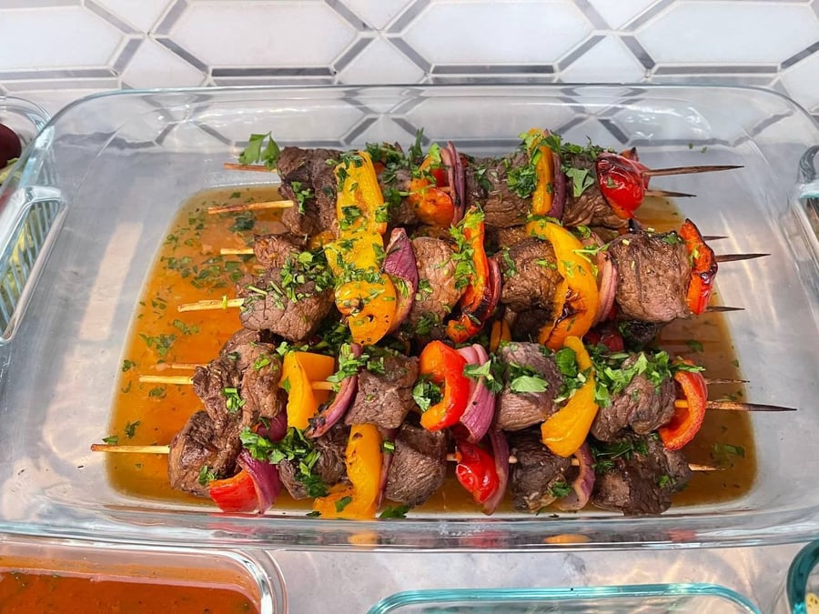 Yellow and orange pepper wedge between beef cubes on six skewers, parsley thrown over the lot.
