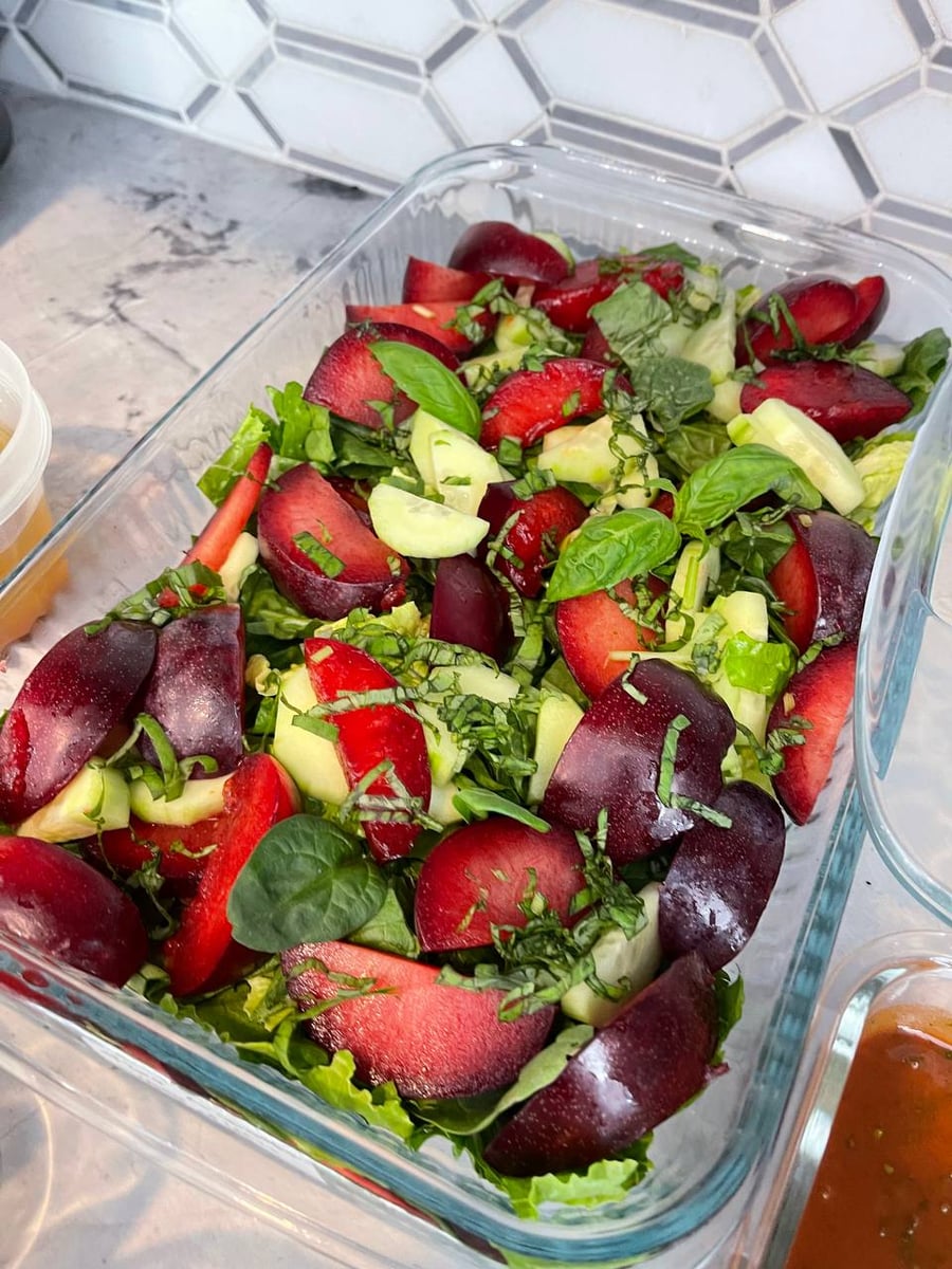 Shredded basil covers plum wedges and strawberries over romaine, cucumber cut through the middle.