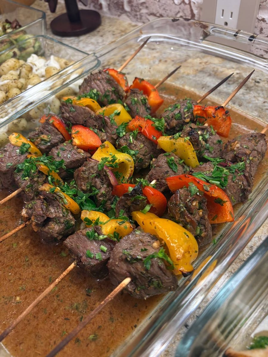 Charred pepper wedges alternate with thick beef sirloin cubes on wooden kebab skewers, all scattered with parsley.