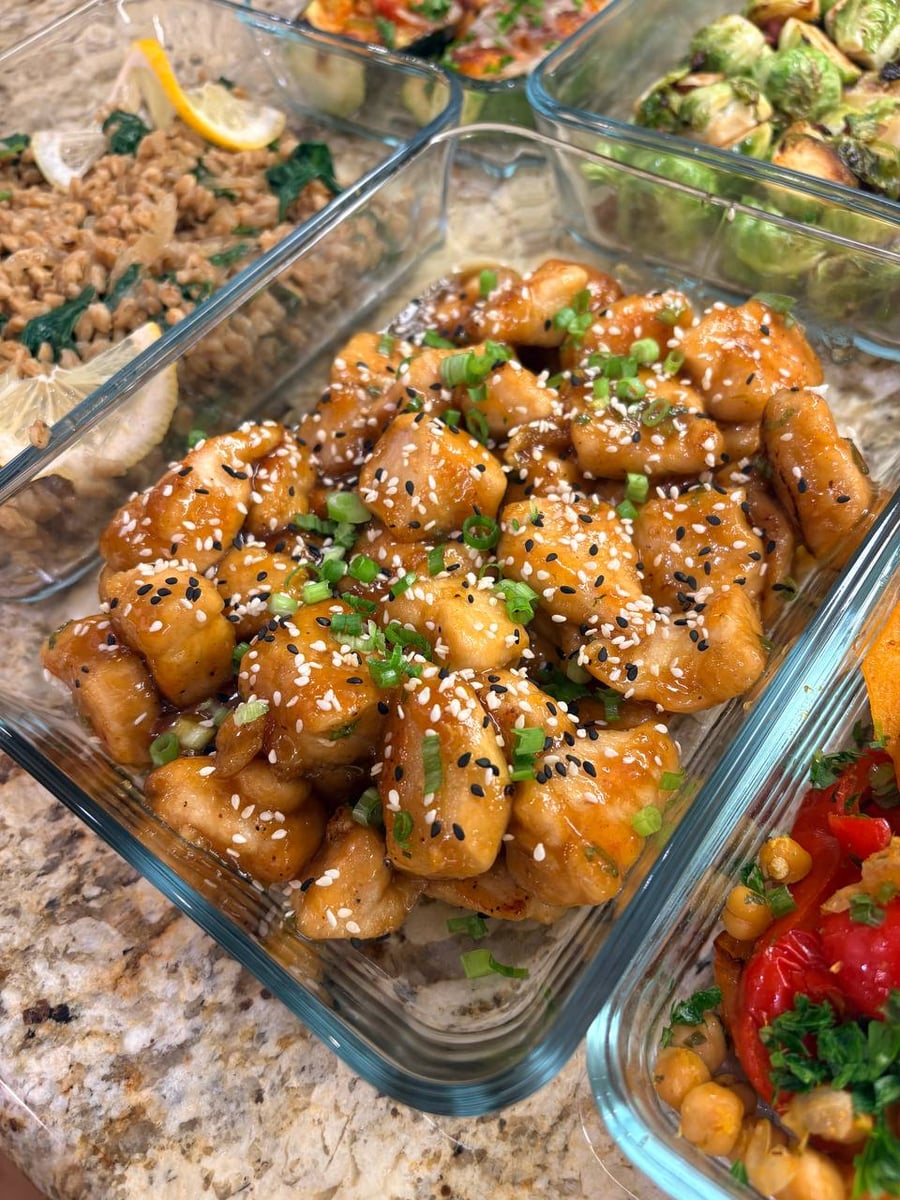 White and black sesame seeds cover glossy honey garlic chicken bites, finished with chopped scallions.