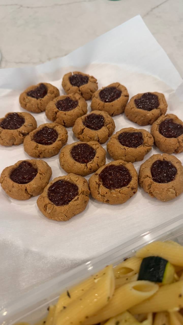 Dark jam pools in each peanut butter thumbprint cookie, cooling on parchment above the penne.