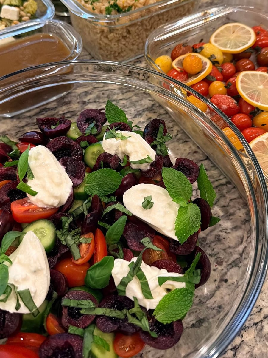 Halved cherries and mozzarella sit among cherry tomatoes, cucumber and mint in a wide bowl.