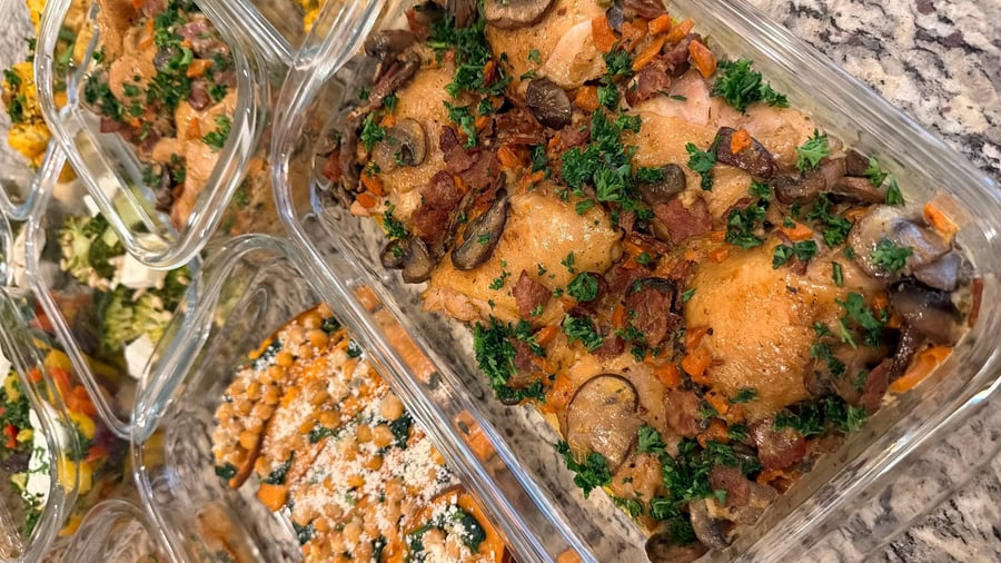 Eighteen containers stacked across granite, coq au vin and stuffed sweet potatoes up top, cherry salad below.