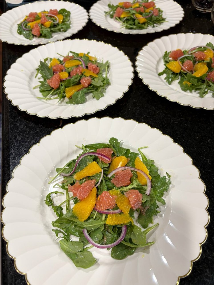 Multiple plates of mixed green salad with citrus and red onion.