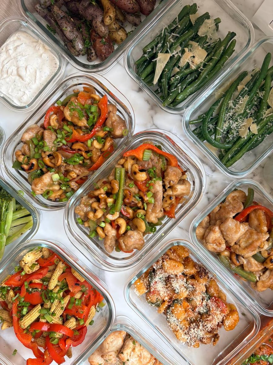 Glossy cashew chicken bites fill three dishes beside baby corn, broccolini, fingerling potatoes and Parmesan green beans.