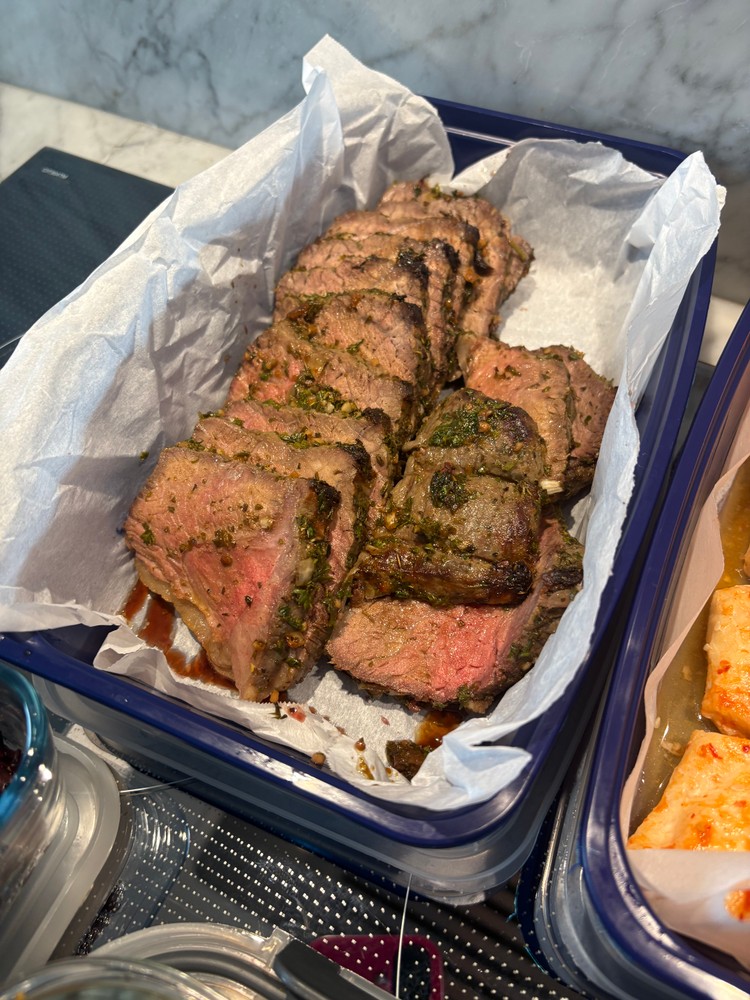 Sliced herb-crusted beef tenderloin in a blue meal prep container.