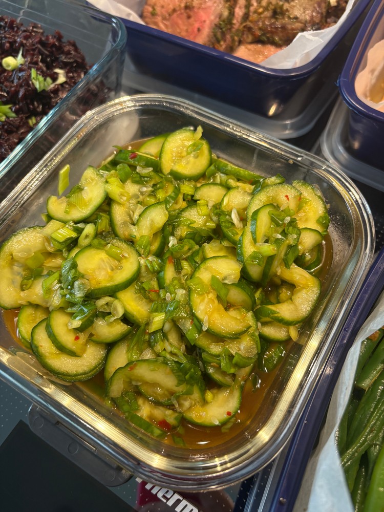 Cucumber salad with scallions and chili flakes in a glass container.