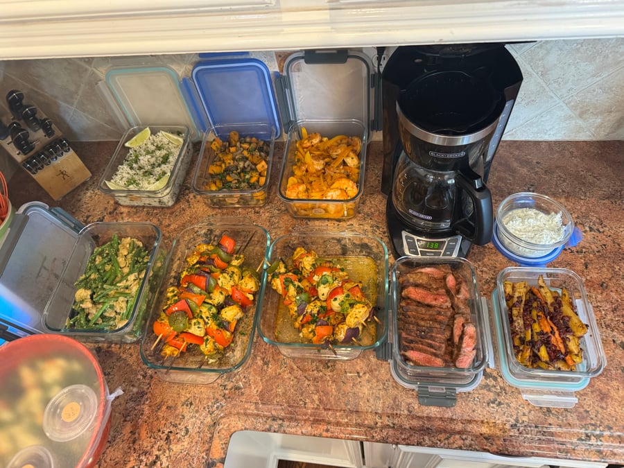 Glass containers filled with chicken skewers, fajita shrimp, sliced NY strip steak, green beans, herbed sweet potatoes, and carrots with yogurt dip.