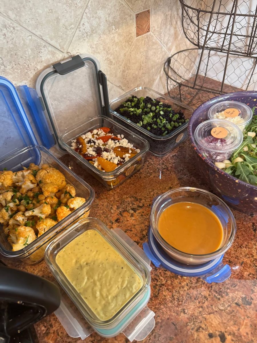 Glass meal prep containers filled with roasted paprika cauliflower, chickpeas, Mediterranean bell peppers with feta, and black rice with fresh scallions for garnish.