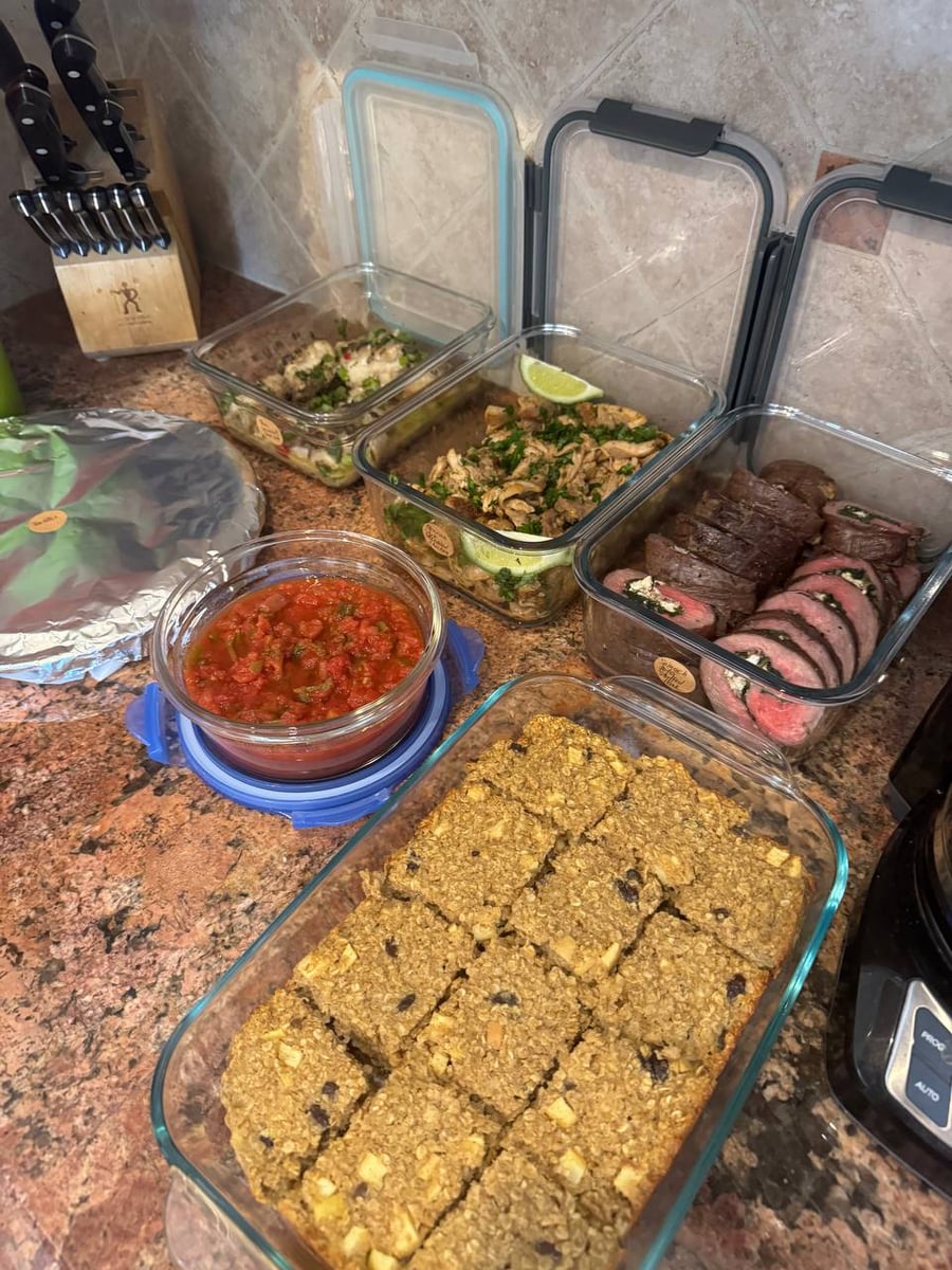 Glass meal prep containers holding sliced spinach-feta stuffed flank steak, Mexican shredded chicken with lime, and a large pan of baked apple cinnamon oats.