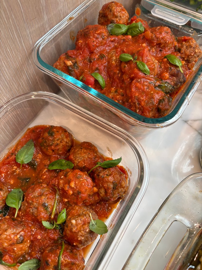 Two glass containers filled with meatballs in marinara sauce, garnished with basil.