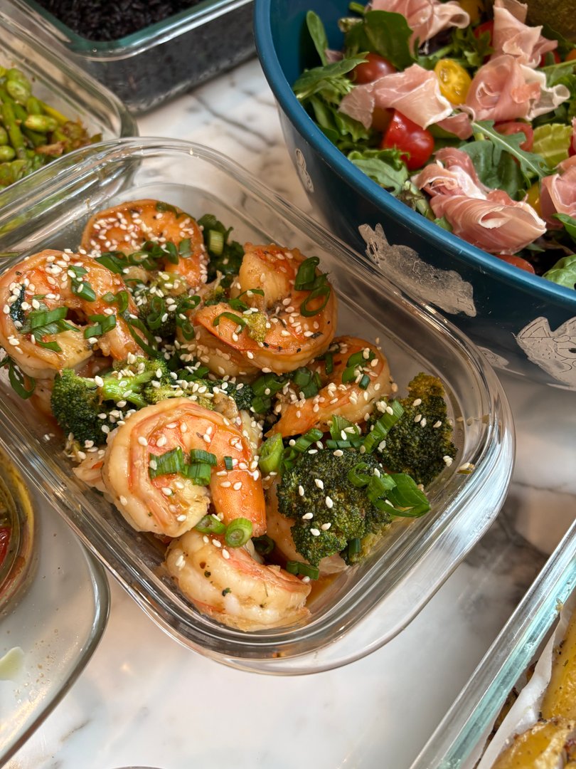 Close-up of sesame shrimp and broccoli in a glass container, garnished with green onions.
