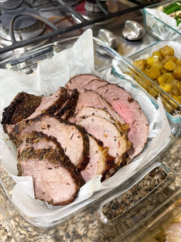 Sliced herb-crusted pork loin in a glass container.