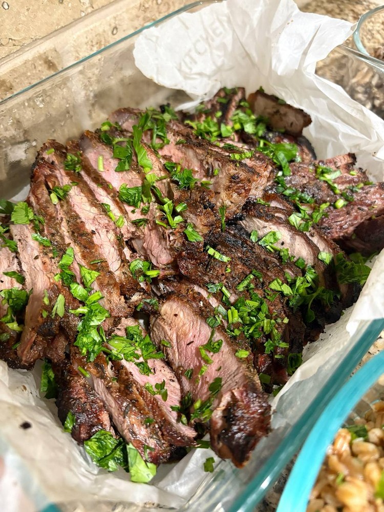 Sliced grilled steak, generously garnished with fresh chopped parsley.