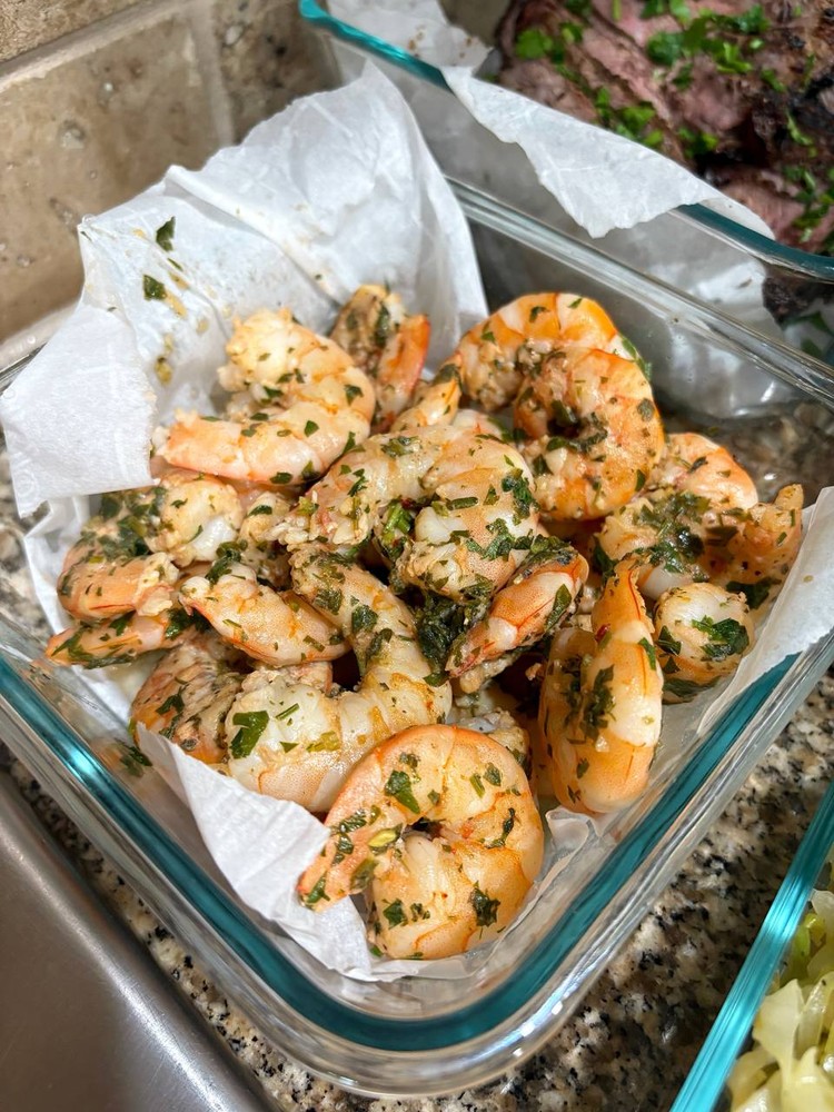 Garlic herb shrimp, cooked and ready in a clear glass container.