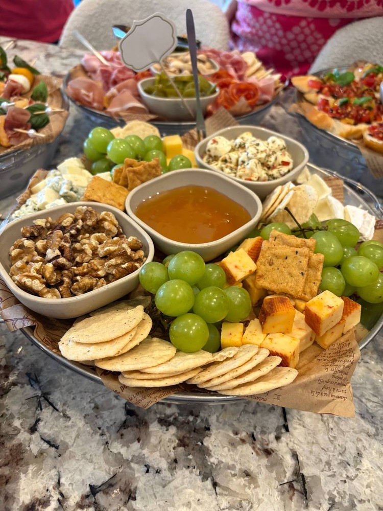 Gourmet cheese platter with grapes, nuts, crackers, and honey.
