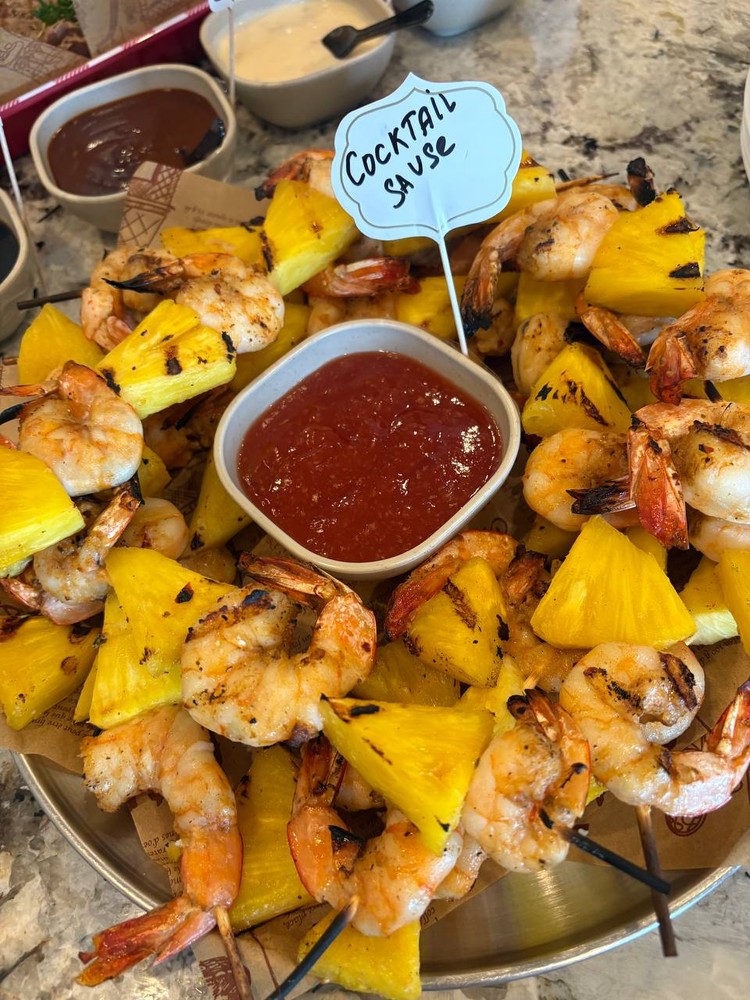 Grilled pineapple and shrimp skewers with cocktail sauce.