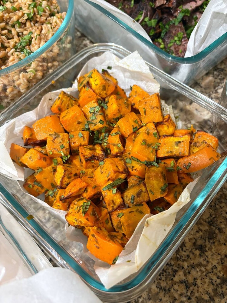 Roasted sweet potato cubes, seasoned with herbs, in a glass dish.