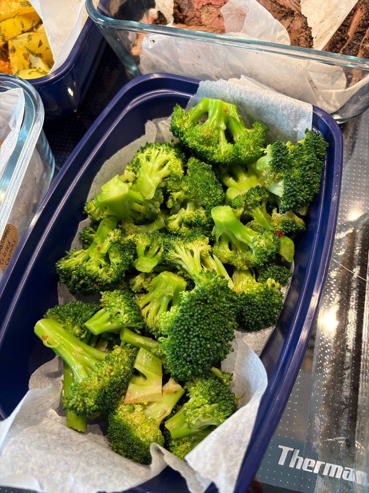 Steamed broccoli florets in a blue meal prep container.