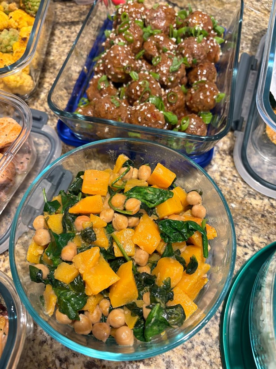 A glass tray of Asian-style beef meatballs garnished with scallions and sesame seeds, alongside a round glass bowl of coconut butternut squash stew with chickpeas and spinach.