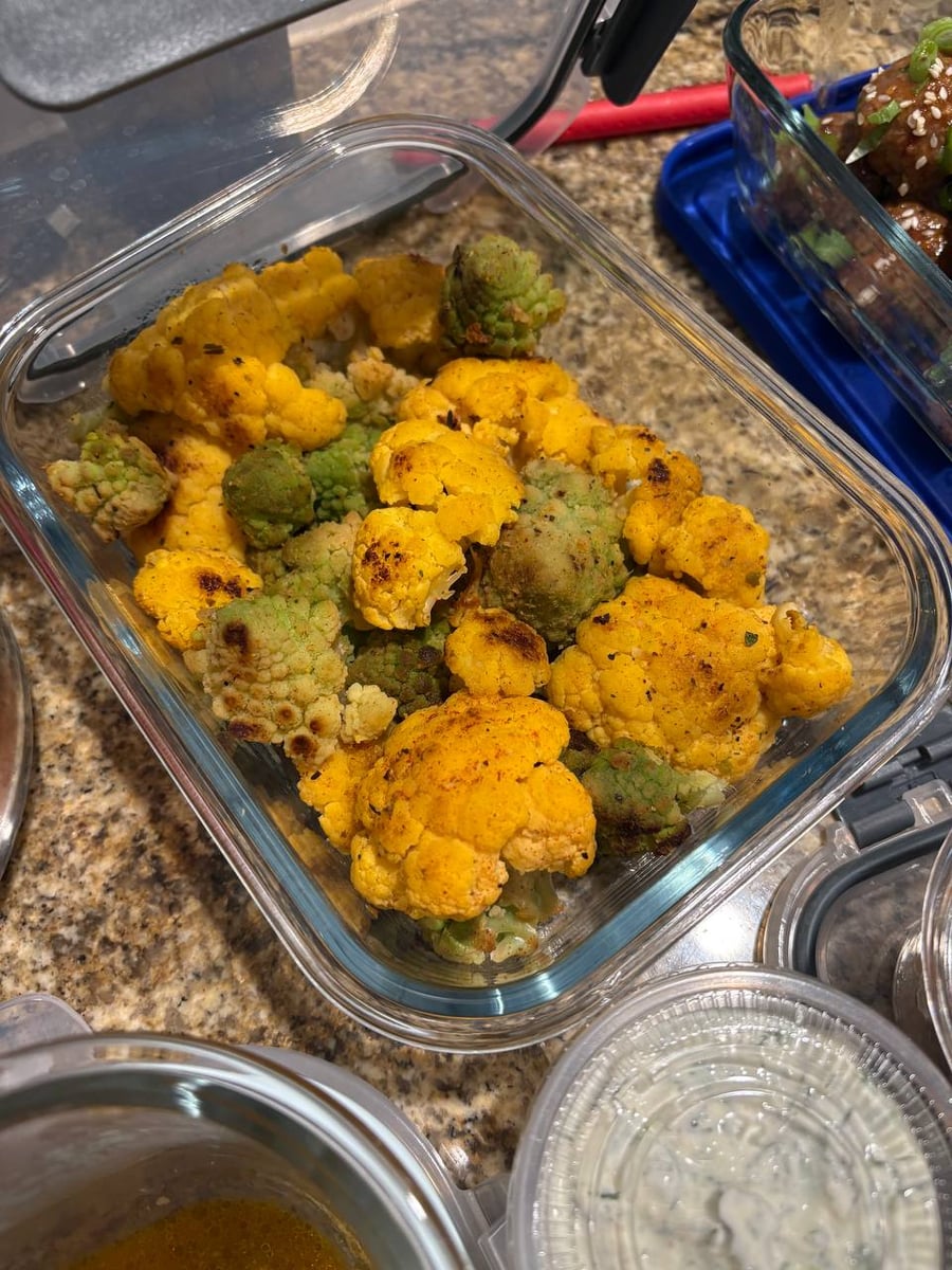 A glass storage container filled with roasted turmeric-seasoned yellow cauliflower and vibrant green romanesco florets, showing a beautiful contrast in textures and colors.