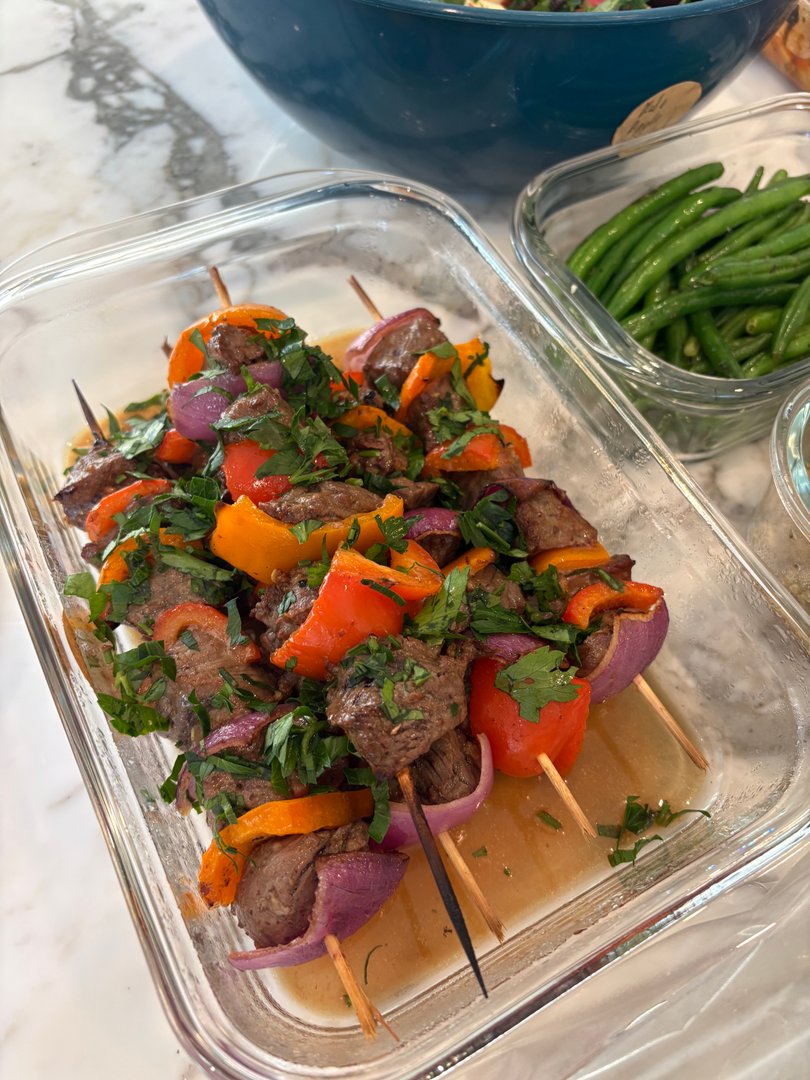 Close-up of beef and vegetable skewers in a glass container, garnished with parsley.