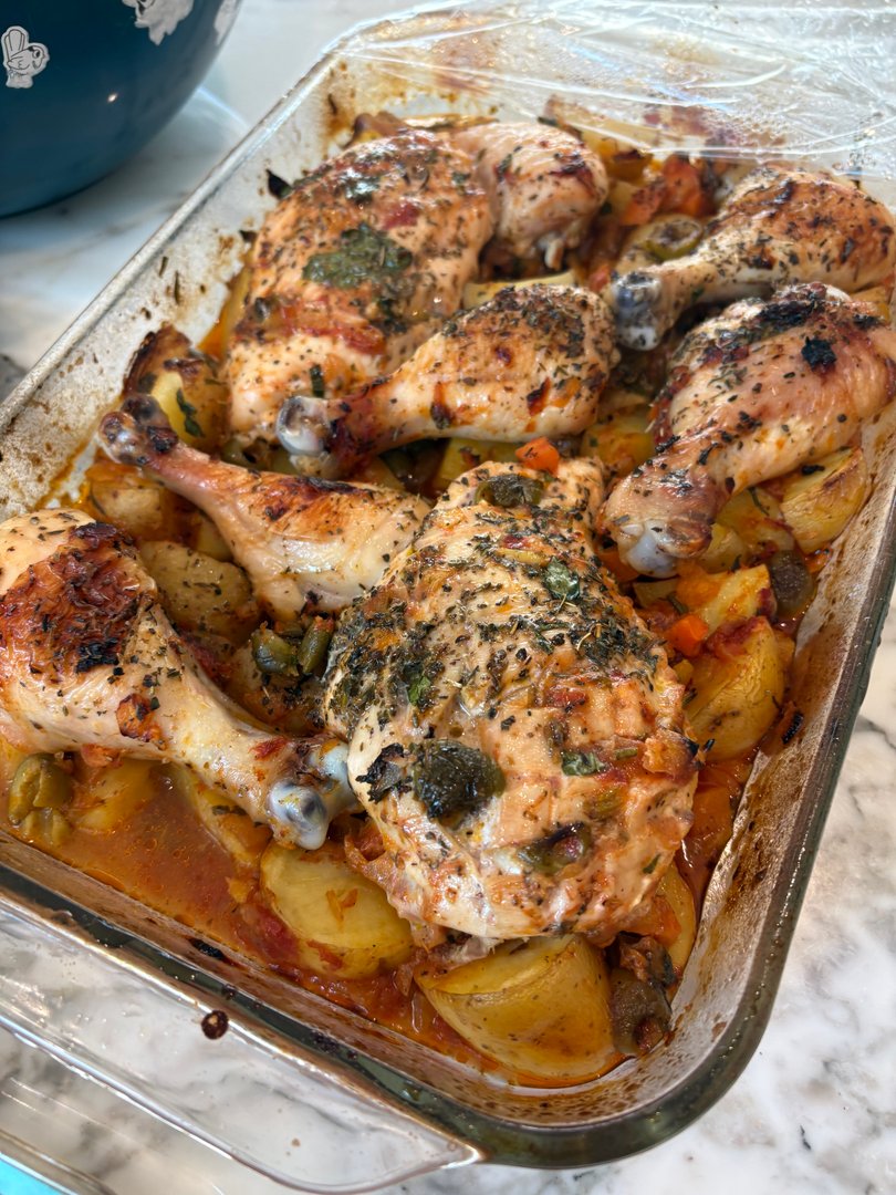 Roasted chicken drumsticks and thighs with potatoes and vegetables in a baking dish.