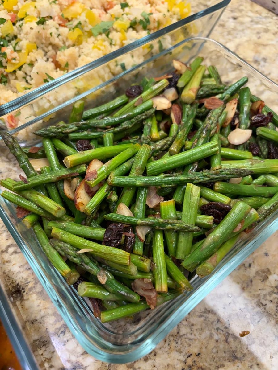 Sliced almonds and dark raisins scatter through charred asparagus, couscous with mixed veggies behind.