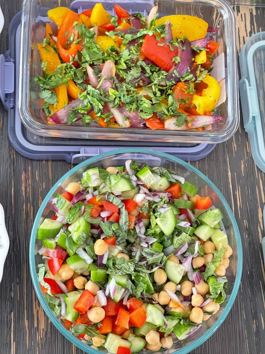Cucumber, chickpeas and red onion sit under torn basil, with cilantro-covered bell peppers and red onions above.