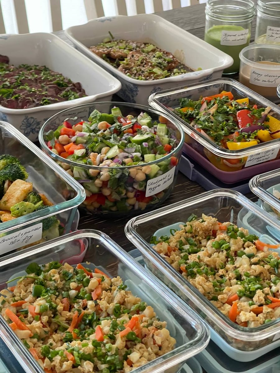 Two floral dishes hold sliced filet mignon and teriyaki chicken, with chickpea cucumber salad and fajita peppers alongside.
