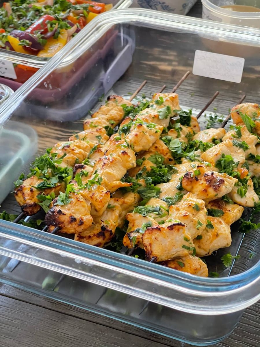 Greek paprika chicken skewers browned at the edges, buried under chopped parsley and cilantro, still on their sticks.