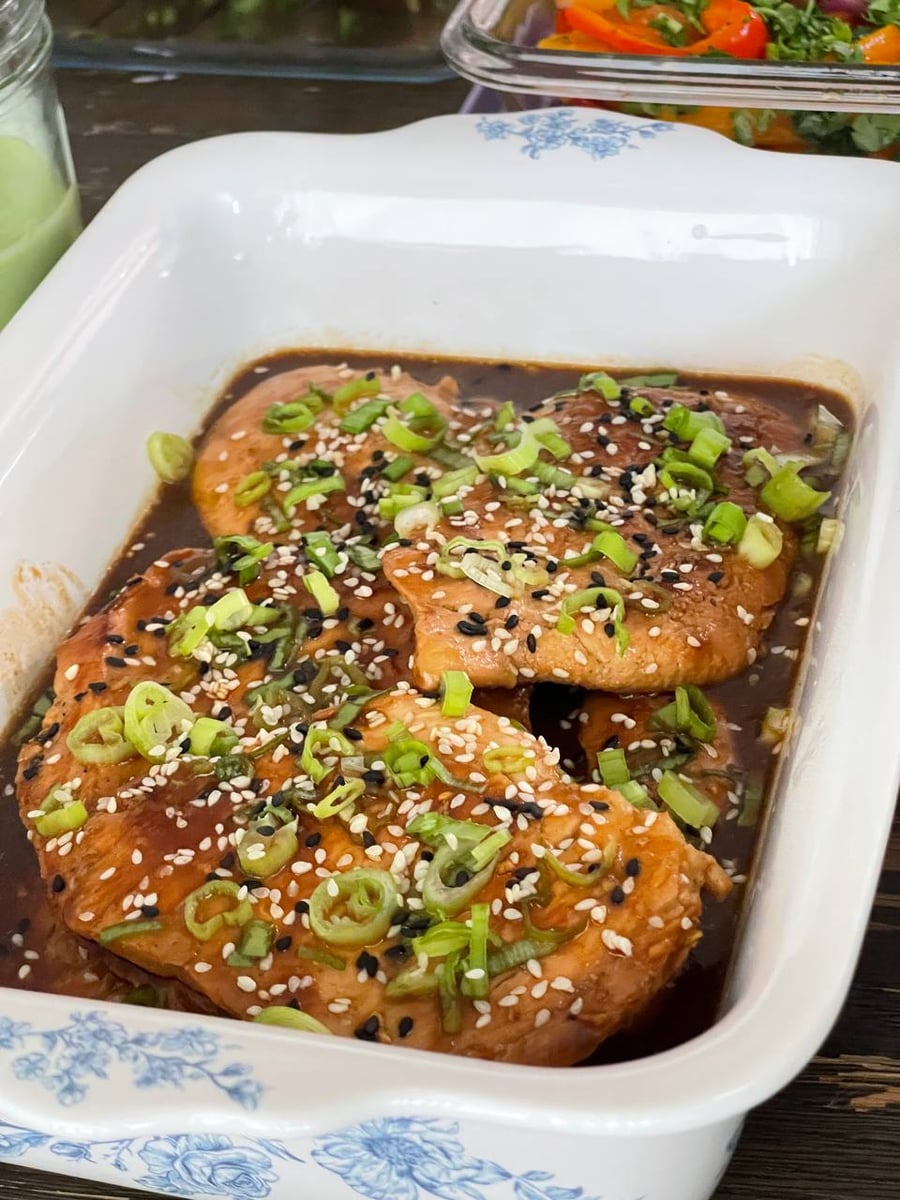 Black and white sesame seeds cover teriyaki chicken sitting in a dark glossy sauce with sliced scallion.