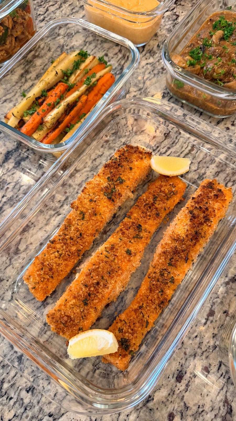 Three panko crusted salmon fillets sit with lemon wedges, parsnips and carrots waiting in the corner.
