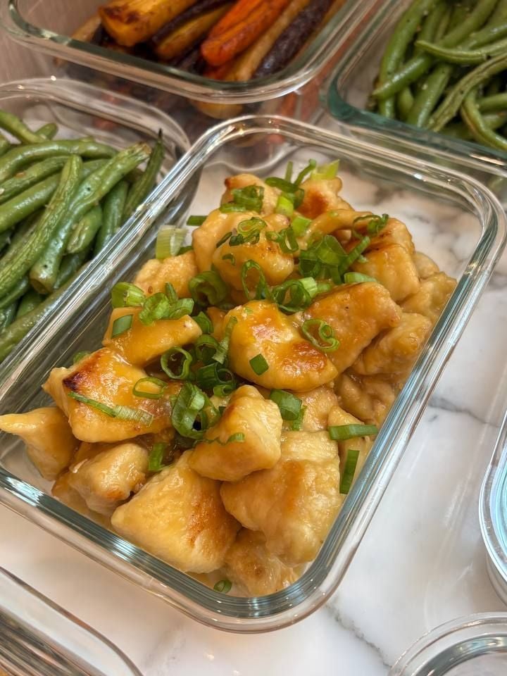 Sliced scallions pile on orange glazed chicken bites, sesame green beans and roasted carrots framing the dish.