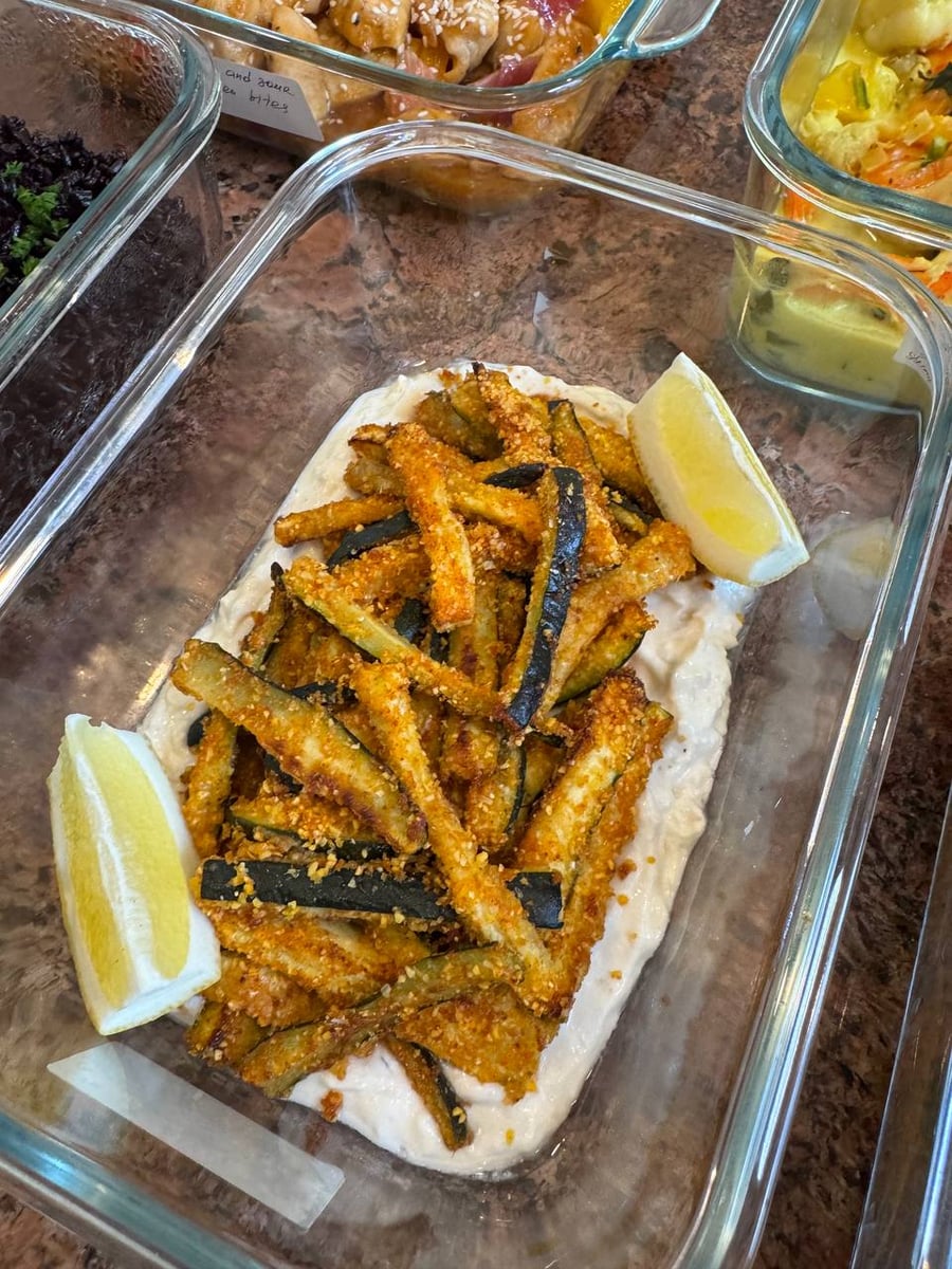 Breadcrumbed zucchini batons pile onto a bed of whipped feta with two lemon wedges tucked in.