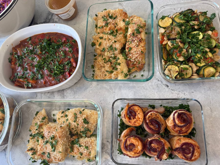 Bacon-wrapped chicken rounds rest on chopped parsley next to white beans with zucchini and red pepper.