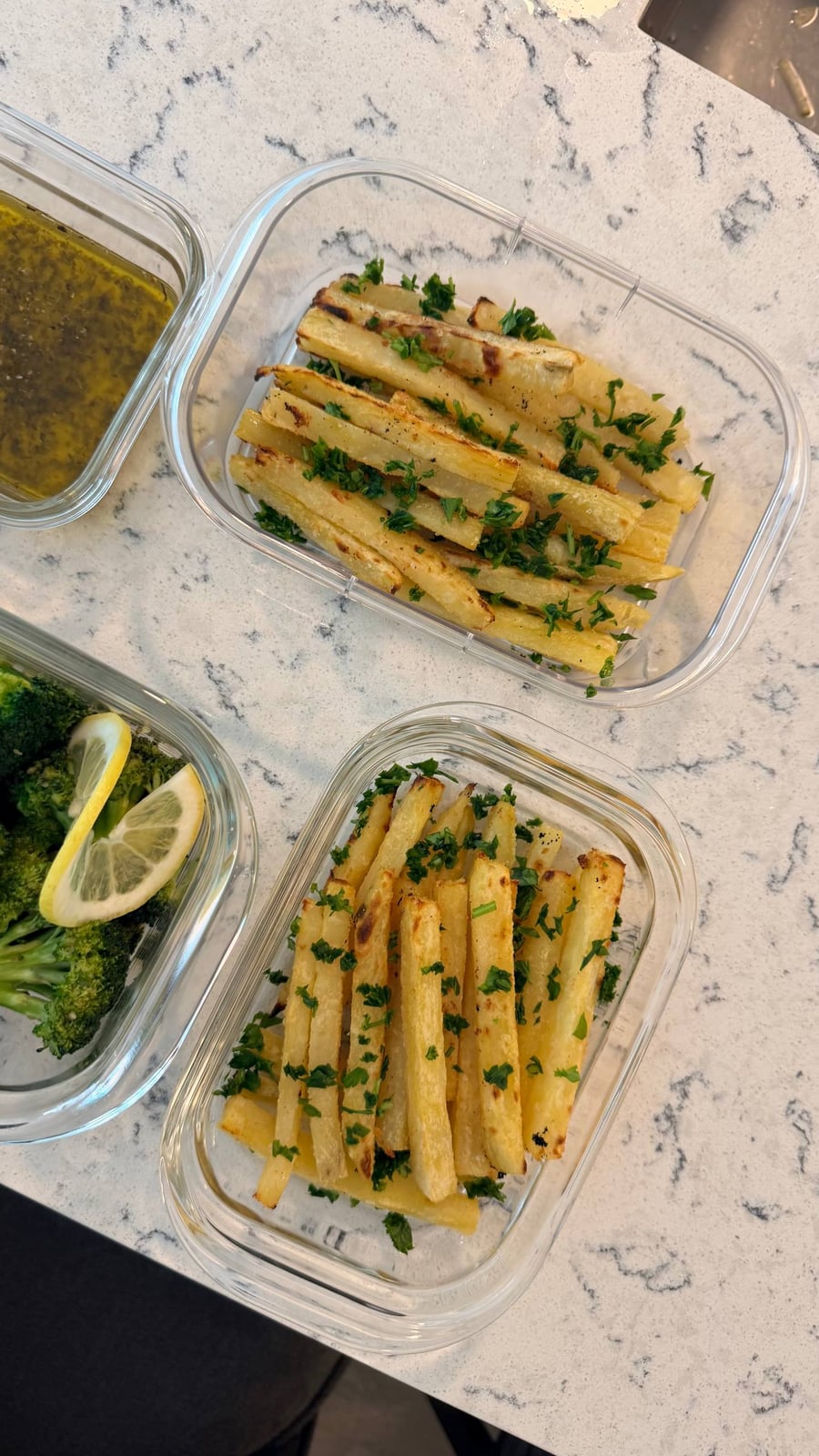 Chopped parsley falls across two trays of parboiled potato fries, maple broccoli and a lemon wheel to the left.