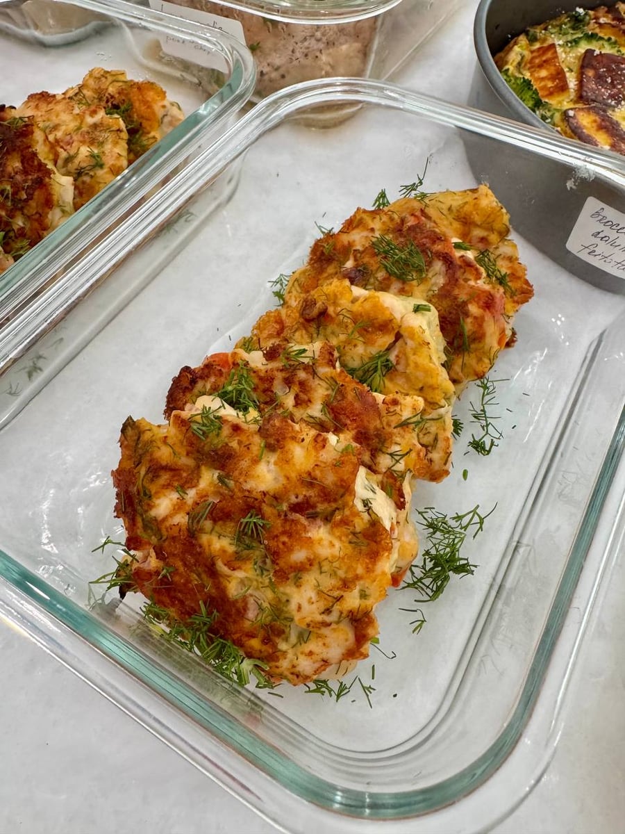 Dill scattered thick over golden chicken patties flecked with tomato, resting in a lined glass tray.