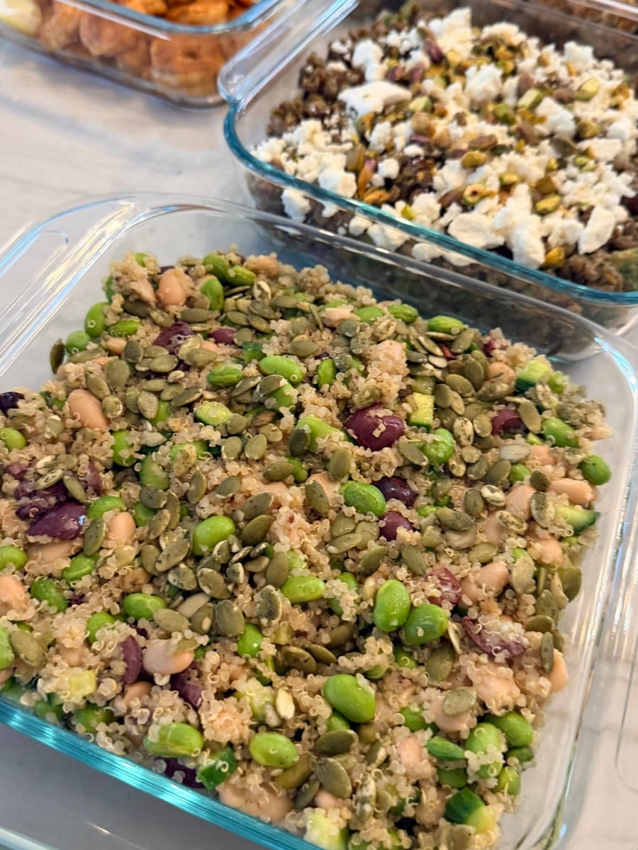 Edamame, white beans and pumpkin seeds fold through cucumber quinoa salad, black lentils and shrimp behind.