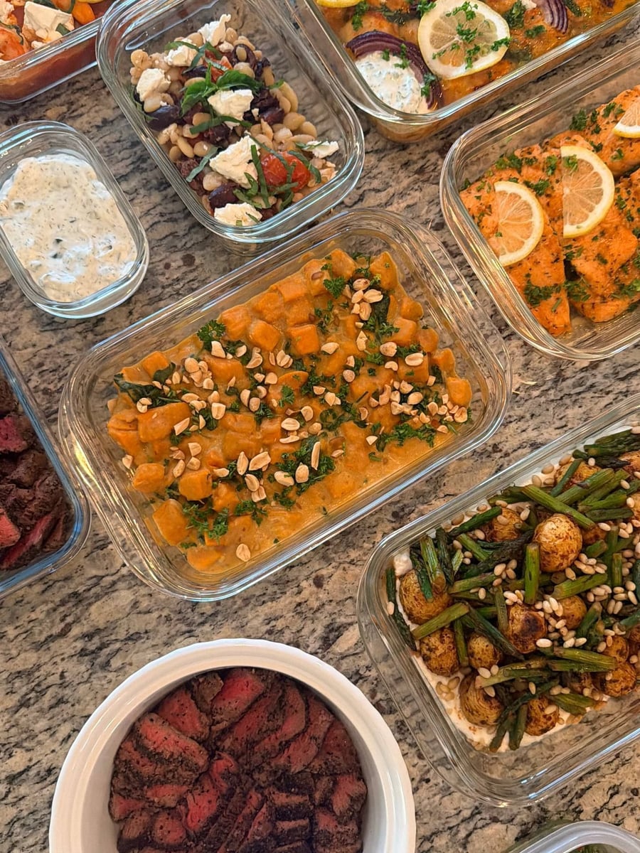 Chopped peanuts scatter over the gingered sweet potato and spinach stew, salmon and shawerma trays behind it.