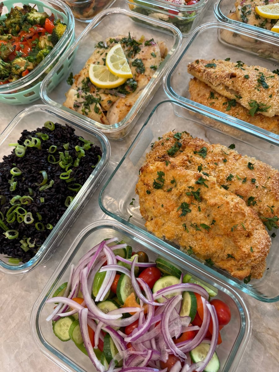 A pale golden crust covers chicken Milano, parsley scattered over, greek salad and black rice beside it.