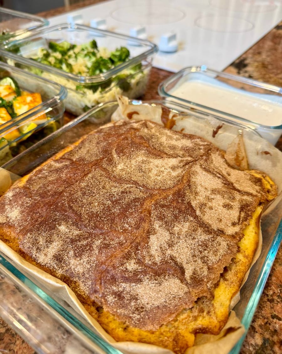 Cinnamon sugar cracks across the top of a coffee cake baked in parchment, broccoli orzo behind it.
