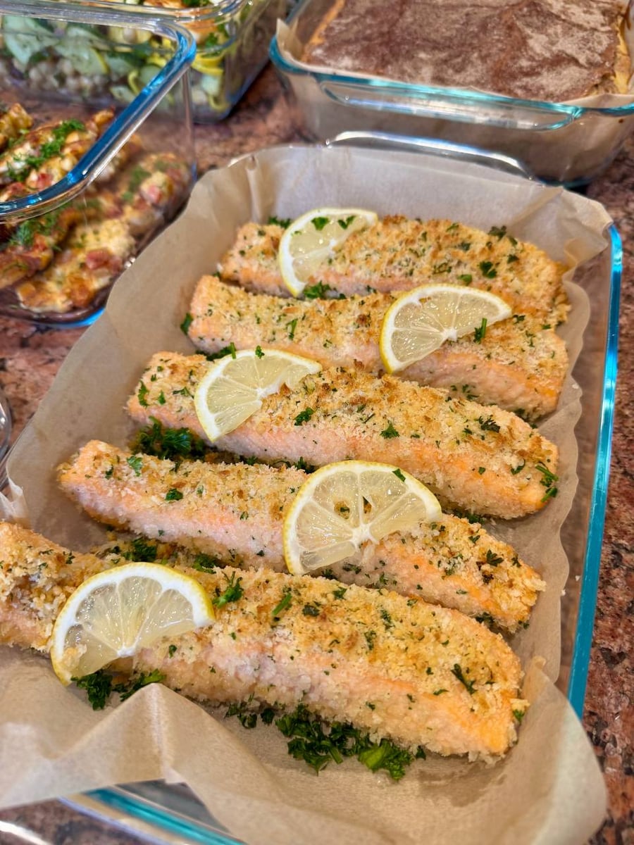 Panko and parsley crust five salmon fillets on parchment, each one topped with a thin lemon wheel.