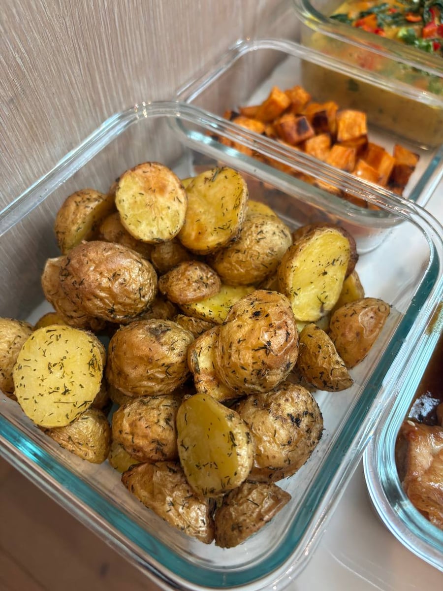 Cut faces of the baby potatoes come up gold and speckled with dill, sweet potato cubes in the tray beyond.