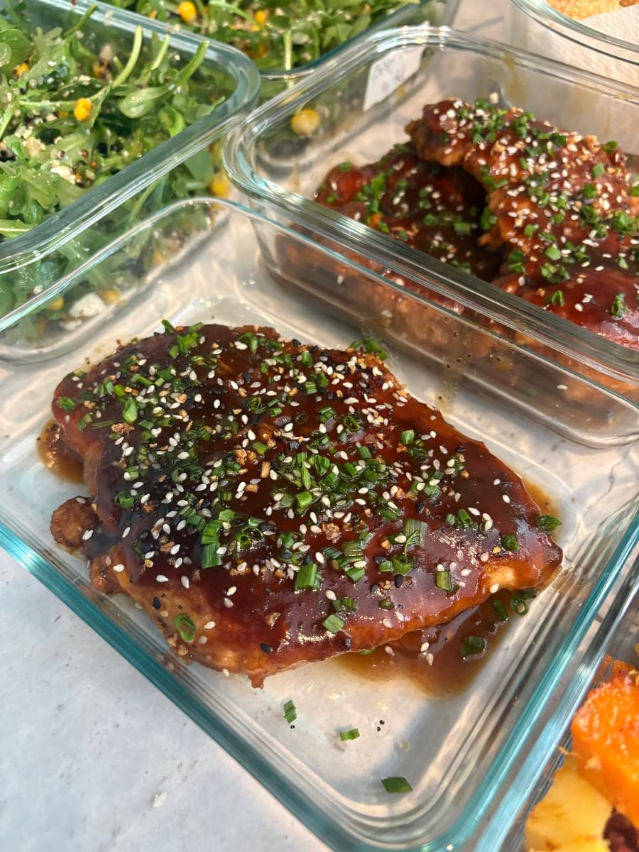 Lacquered teriyaki glaze holds white sesame seeds and chopped chives across the chicken breast, arugula salad behind.
