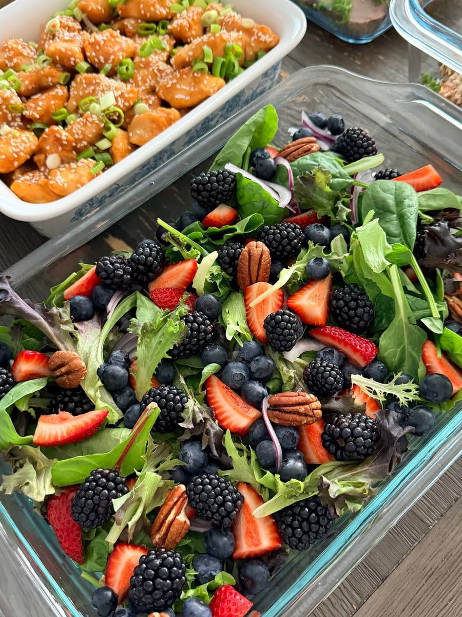 Blackberries, blueberries and strawberry halves crowd the spring mix with pecans, orange glazed chicken bites above.