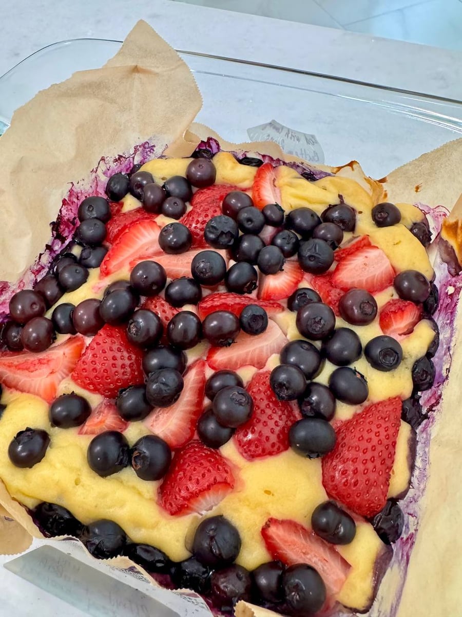 Blueberries and strawberry halves press into the baked protein bun, still sitting on its parchment.
