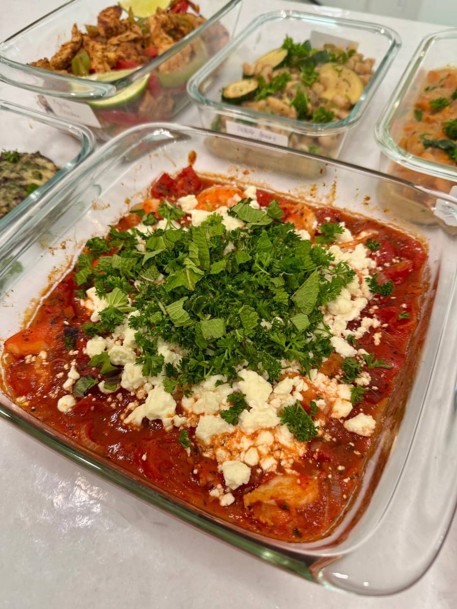 Mint and parsley heap over crumbled feta on the shrimp saganaki, tomato dark underneath it.