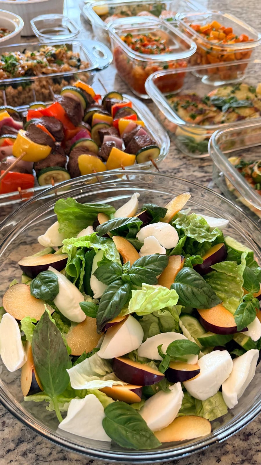 Torn mozzarella, plum slices and basil crowd a glass bowl over romaine and cucumber.